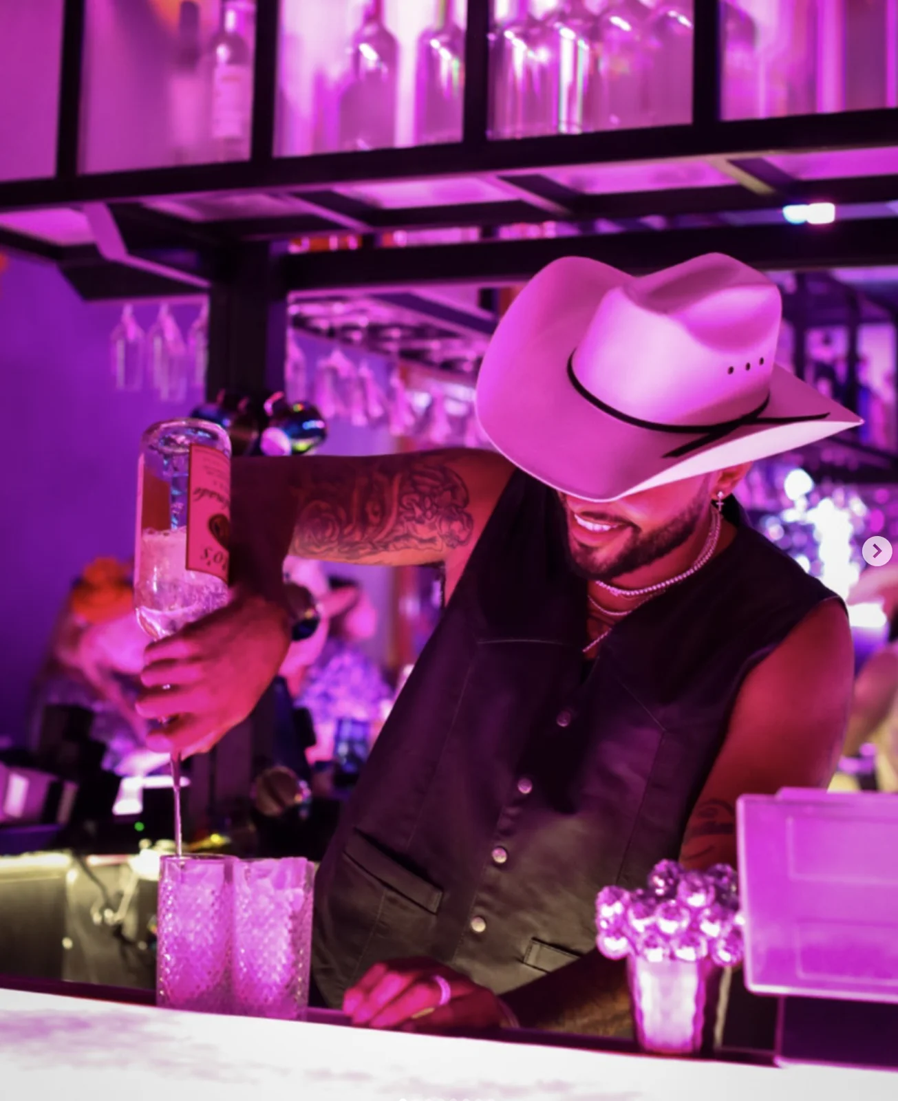 A bartender making a long pour under magenta lights at Lola’s Liquors